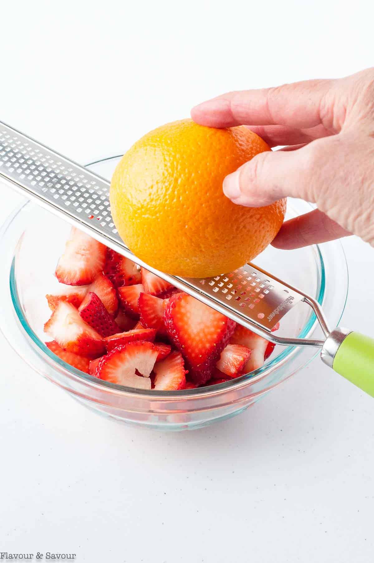 Grating orange zest onto sliced strawberries.