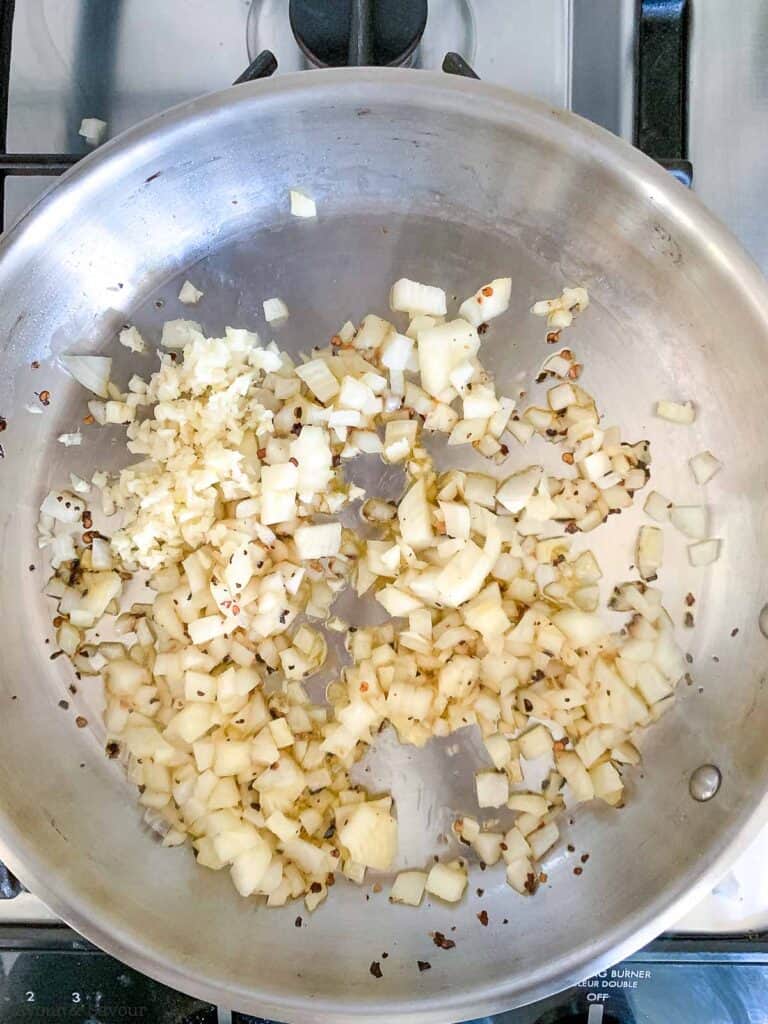 Sauté onion and minced garlic in a skillet to make arrabbiata sauce.