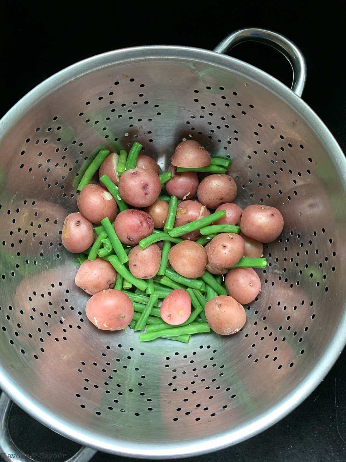 draining cooking green beans and baby potatoes in a colander.
