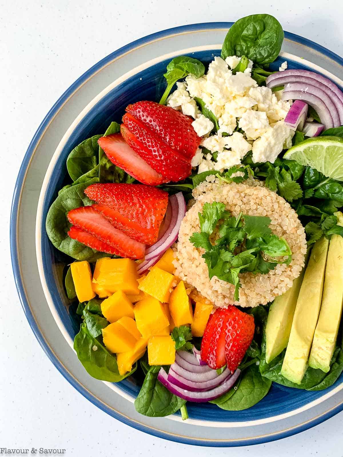 close up view of quinoa bowl with spinach, feta and strawberries.