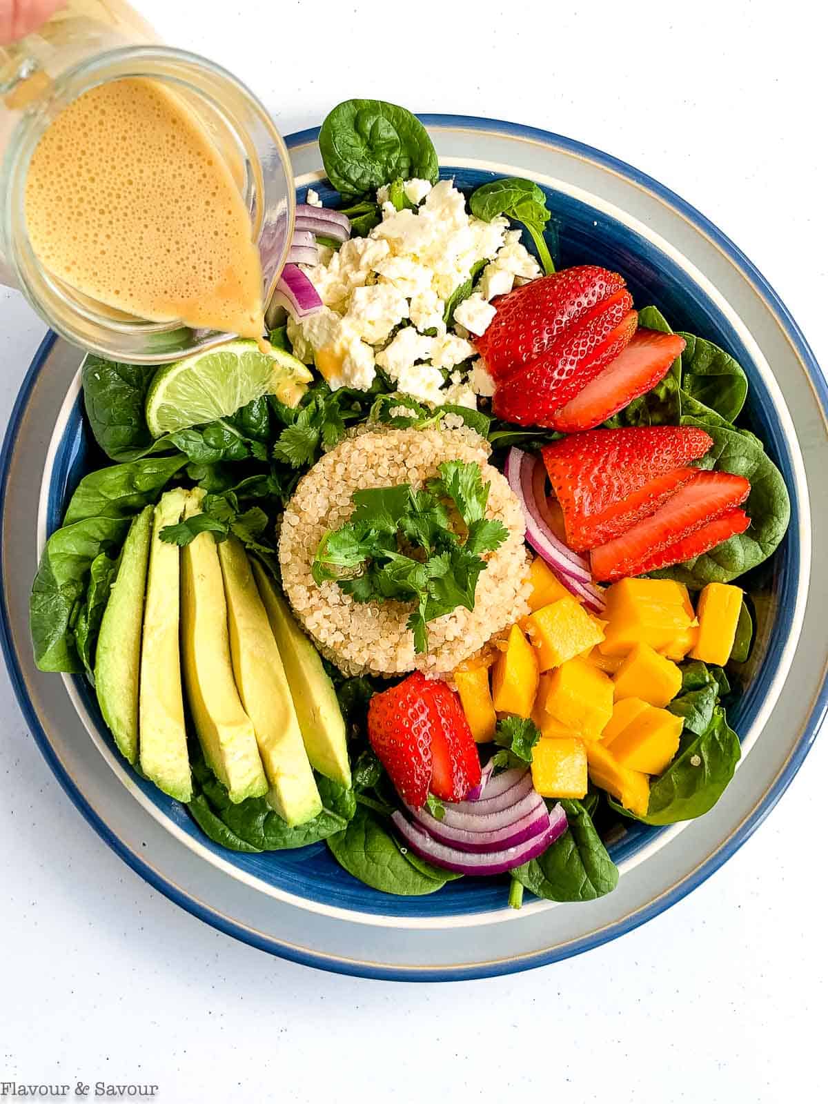 Overhead view of quinoa bowl with spinach, feta and strawberries with dressing.