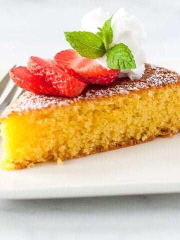 A slice of one-bowl flourless lemon almond cake topped with strawberries and a mint leaf.