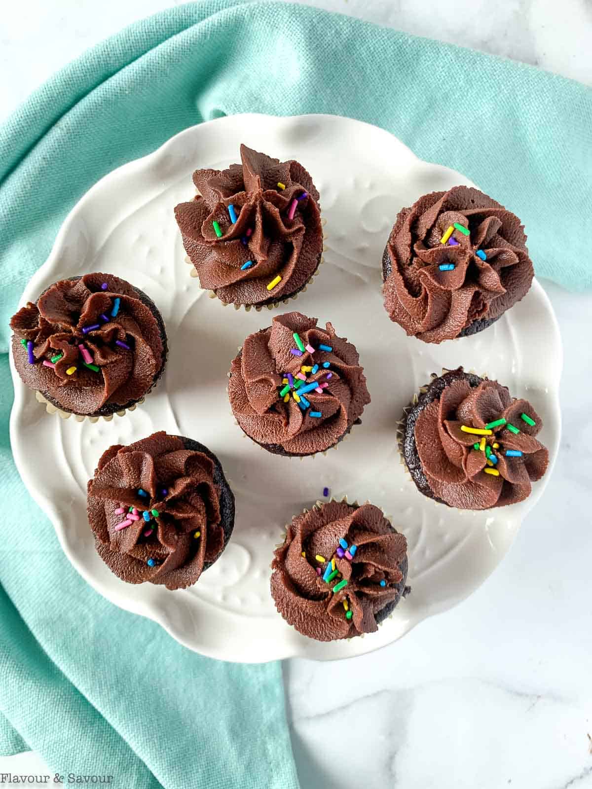 Mini chocolate quinoa cupcakes with chocolate coconut frosting and sprinkles on a white plate.