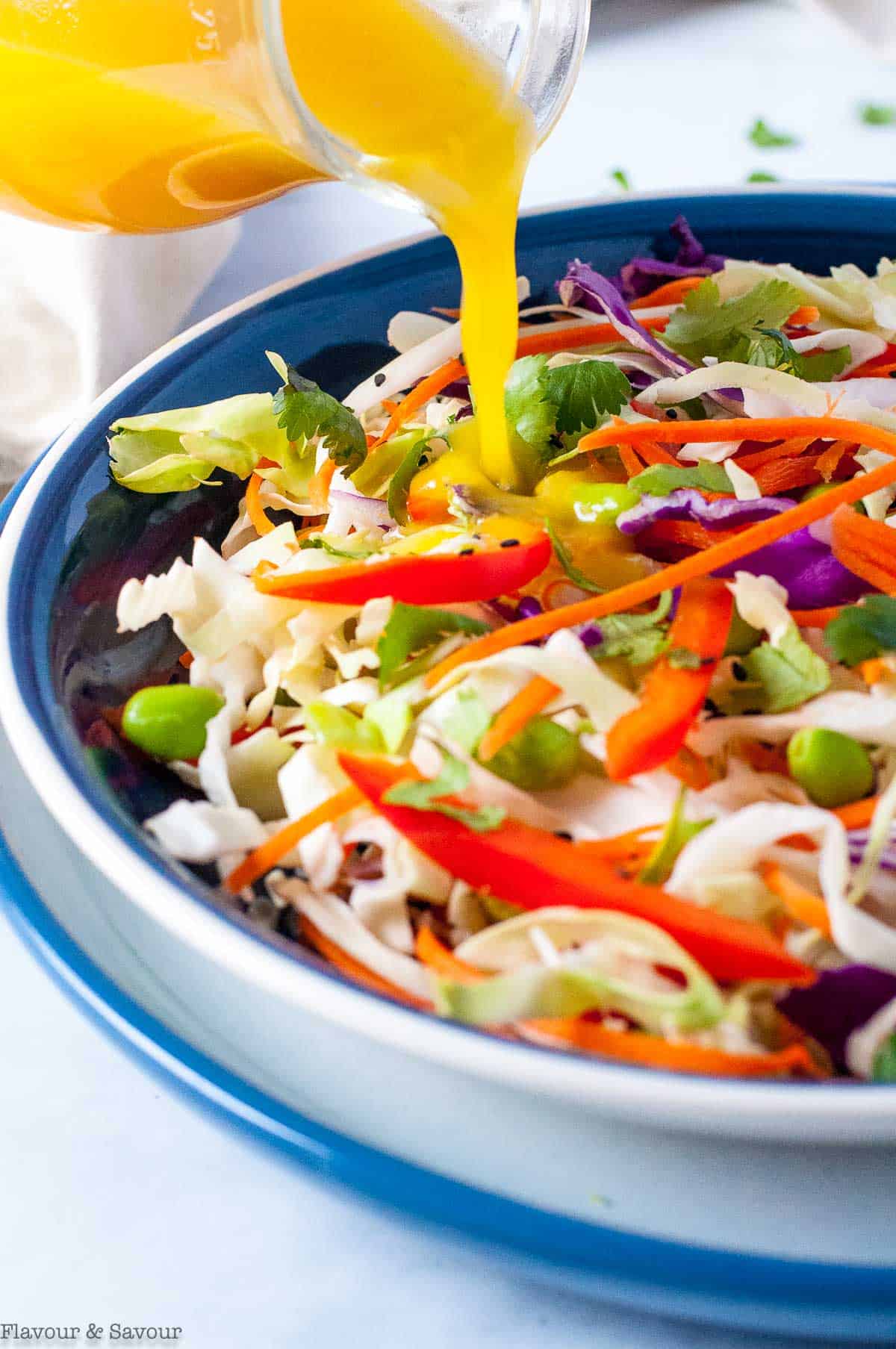 pouring ginger orange dressing on coleslaw.