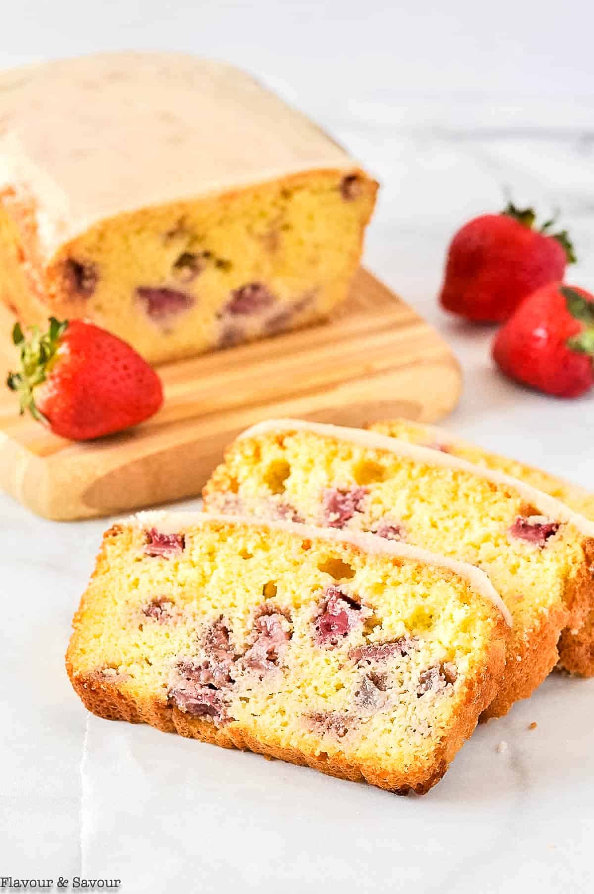 A loaf of gluten-free strawberry lemon loaf with slices and fresh strawberries.
