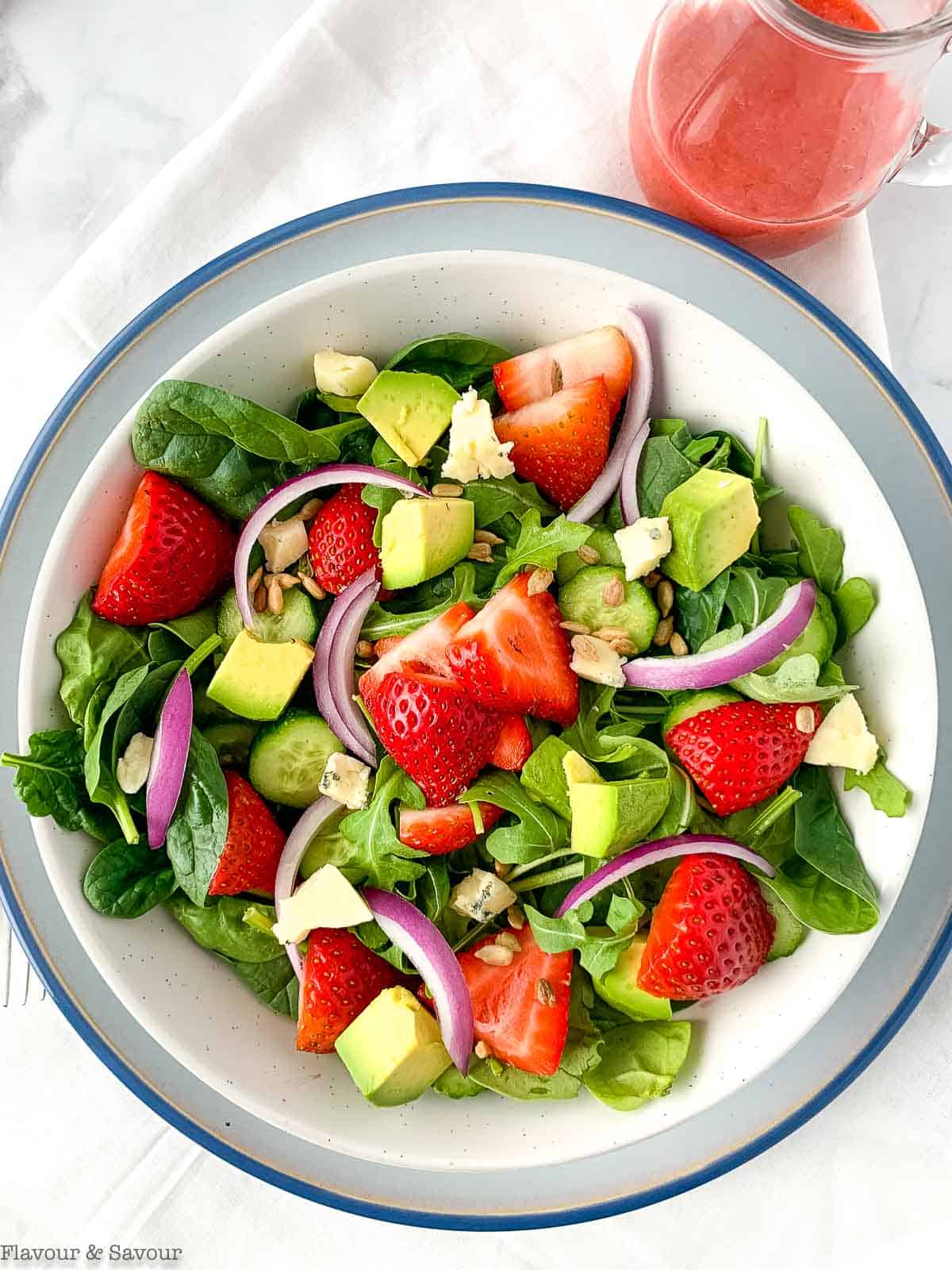 A bowl of strawberry spinach salad with avocado and red onion.