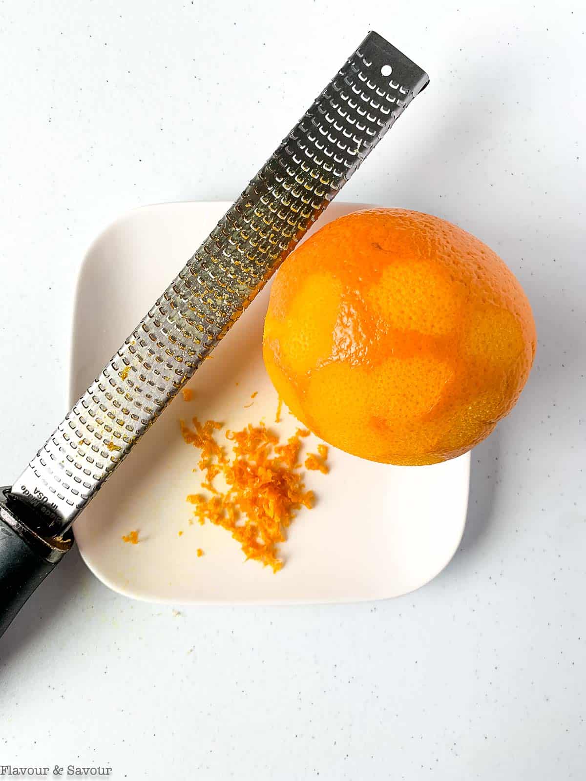 an orange, orange zest and a zester.