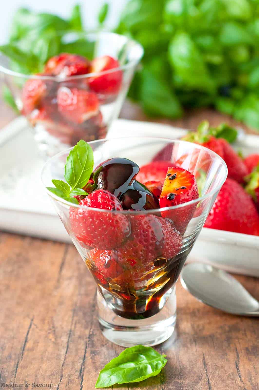 A glass dessert dish with strawberries and balsamic glaze.