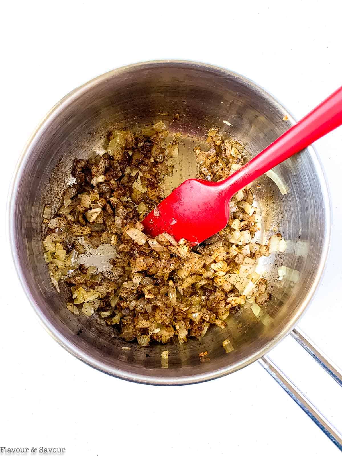 Adding chili powder to onions and garlic in a saucepan.