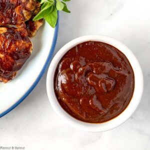 a small bowl of cherry barbecue sauce near grilled chicken.