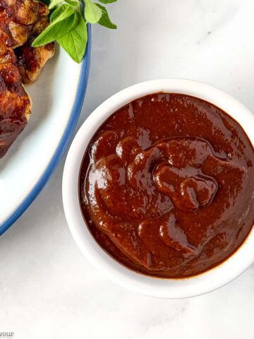 a small bowl of cherry barbecue sauce near grilled chicken.