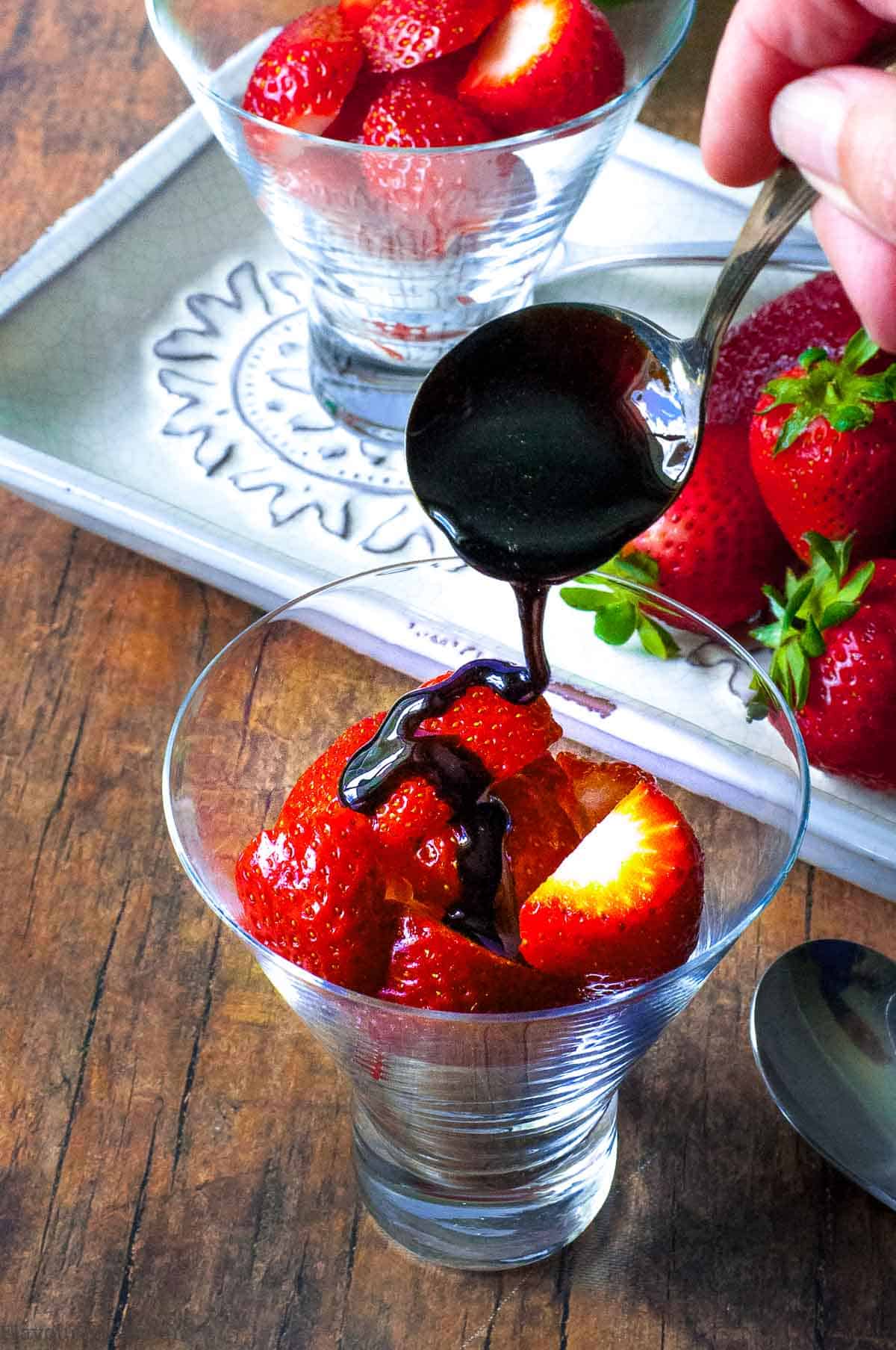 Drizzling balsamic glaze on strawberries in a glass dessert dish.