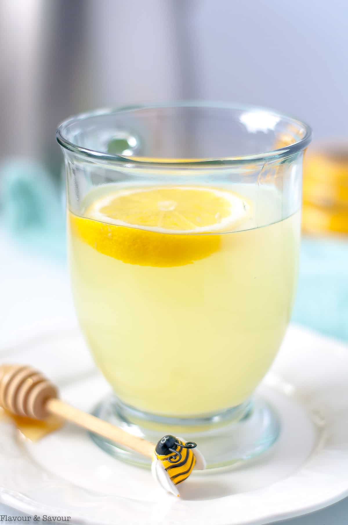 A glass mug with lemon ginger tea and a slice of lemon.