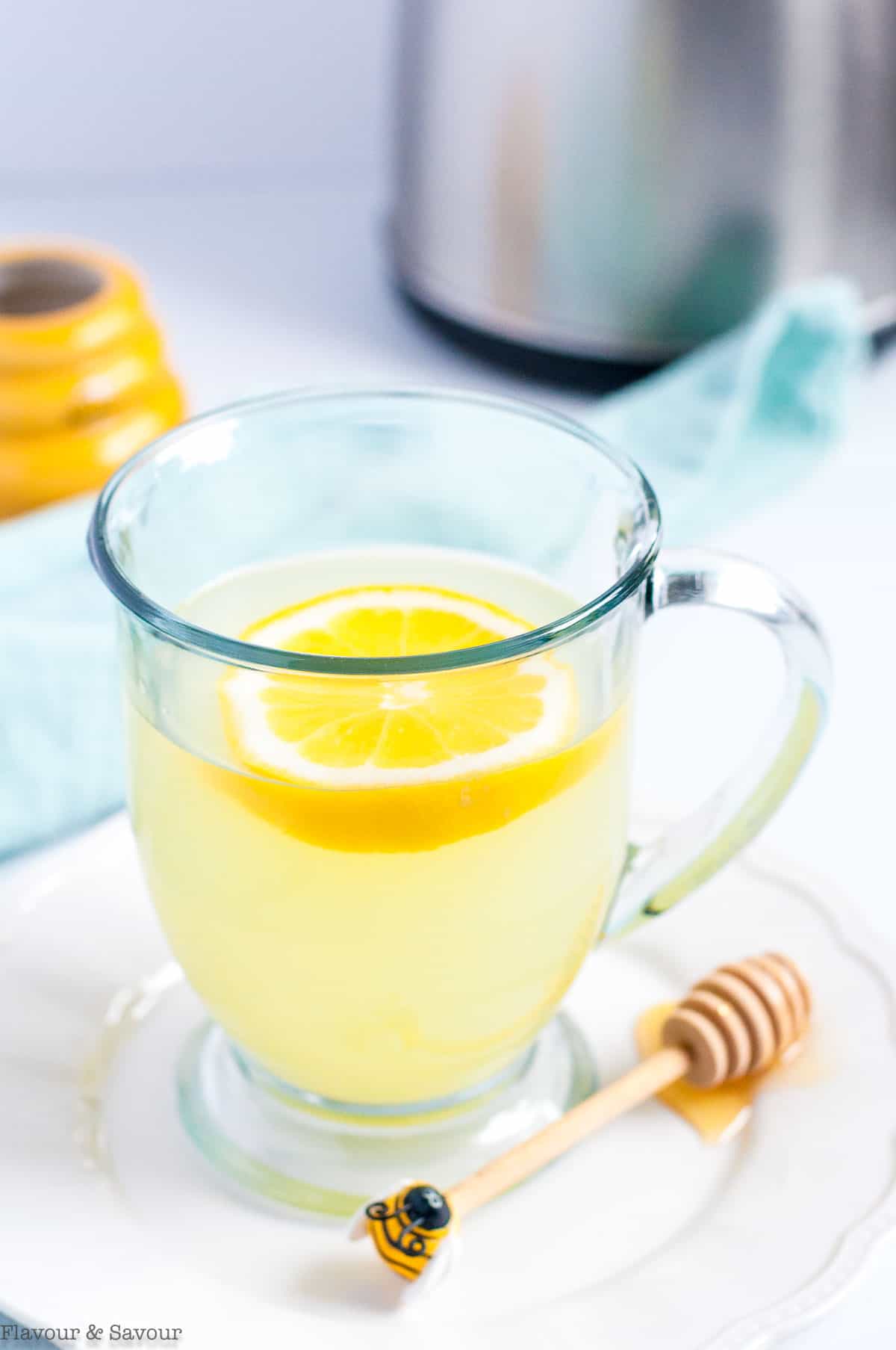 A clear glass mug of lemon ginger tea with a honey spoon.