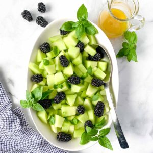 Overhead view of an oval bowl filled with honeydew blackberry salad with basil.