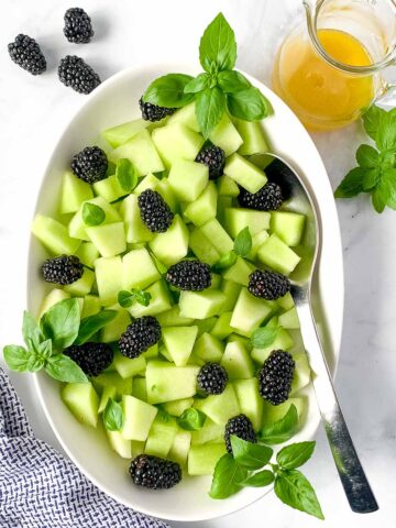 Overhead view of an oval bowl filled with honeydew blackberry salad with basil.