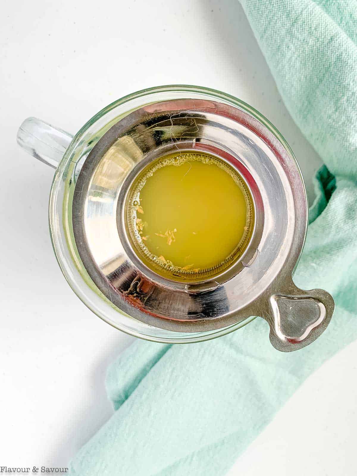 Lemon ginger tea steeping in a tea strainer in a mug.