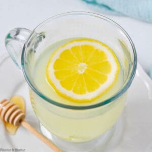 A glass mug of lemon ginger tea with a lemon slice.