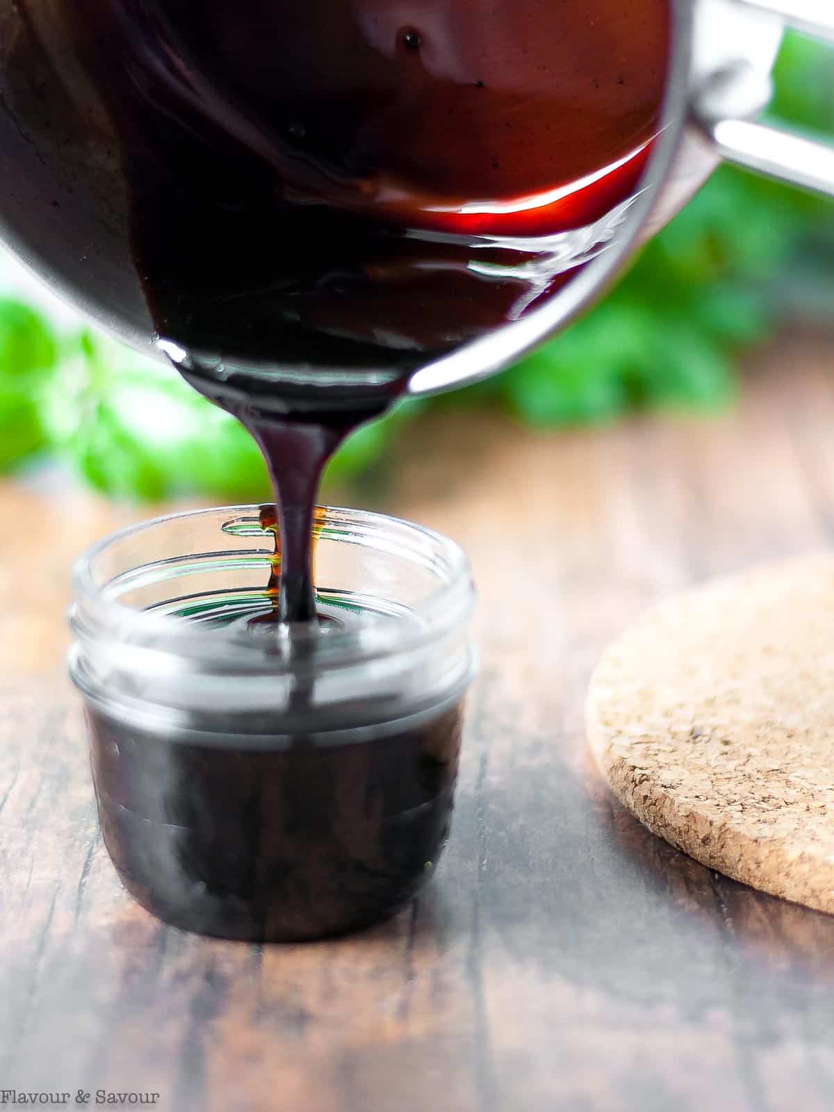 Pouring balsamic glaze into a jar from a saucepan.