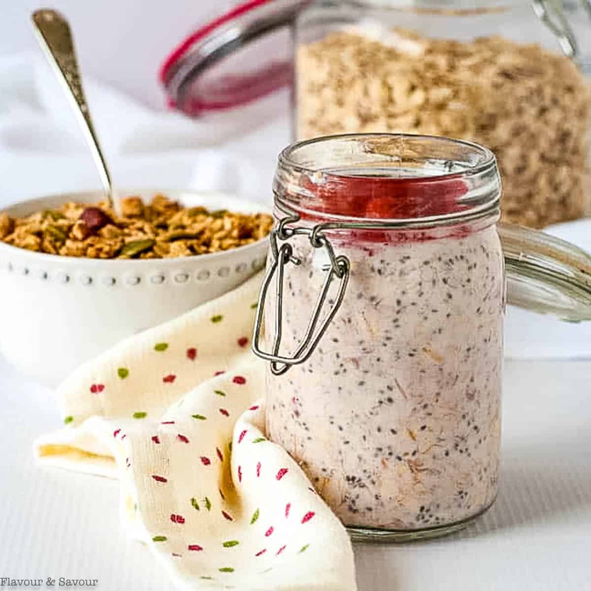 Strawberry rhubarb overnight oats in a glass jar with granola in the background.