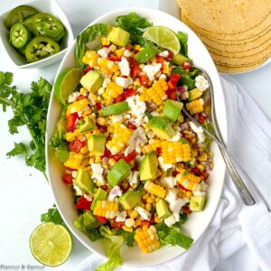 A bowl of Mexican corn salad with a small dish of slice jalapeños beside.