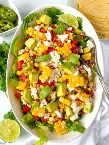 A bowl of Mexican corn salad with a small dish of slice jalapeños beside.