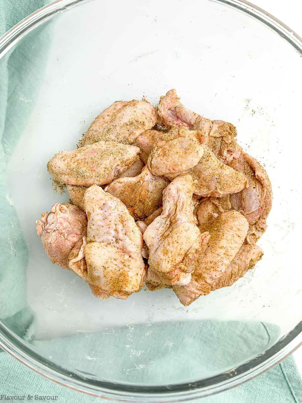 Raw chicken wings in a glass bowl with Old Bay seasoning.