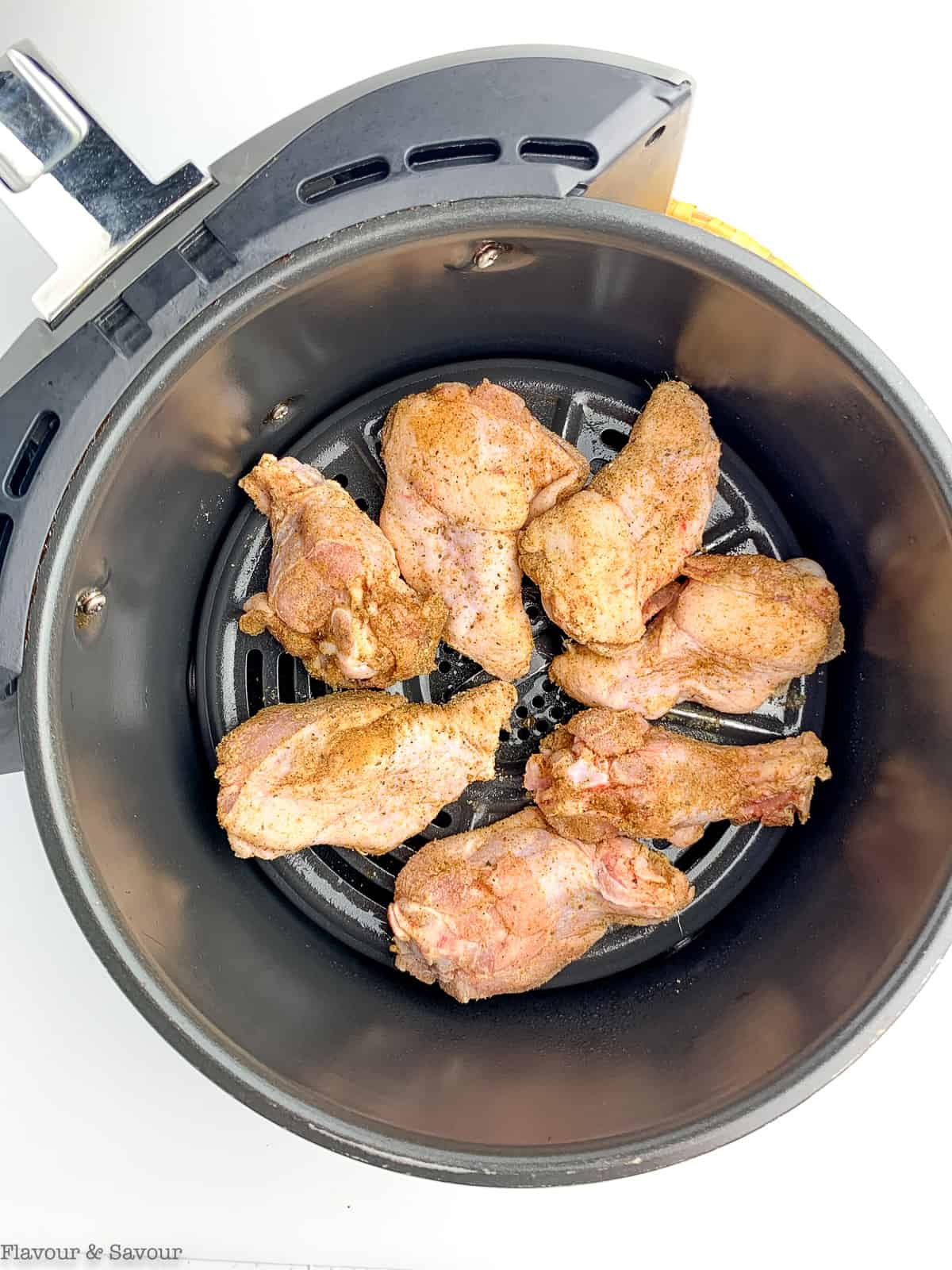 Raw chicken wings in an air fryer basket.