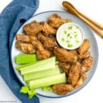A round plate with Old Bay Chicken Wings cooked in an air fryer, blue cheese dip and celery sticks.