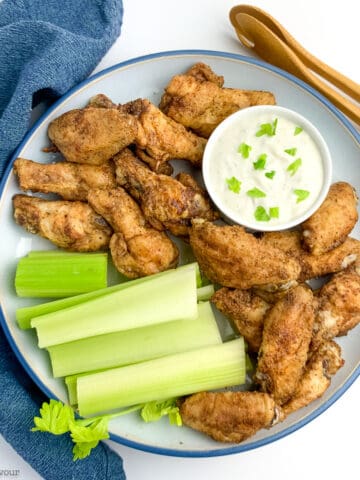A round plate with Old Bay Chicken Wings cooked in an air fryer, blue cheese dip and celery sticks.