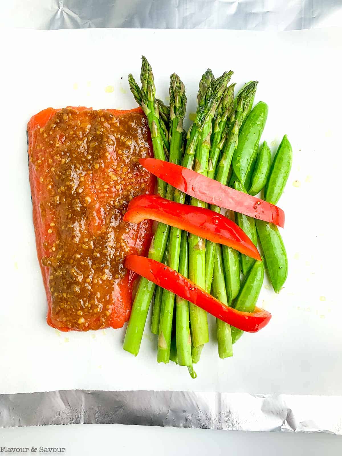 Miso glazed salmon and asparagus on a sheet of foil lined with parchment paper.