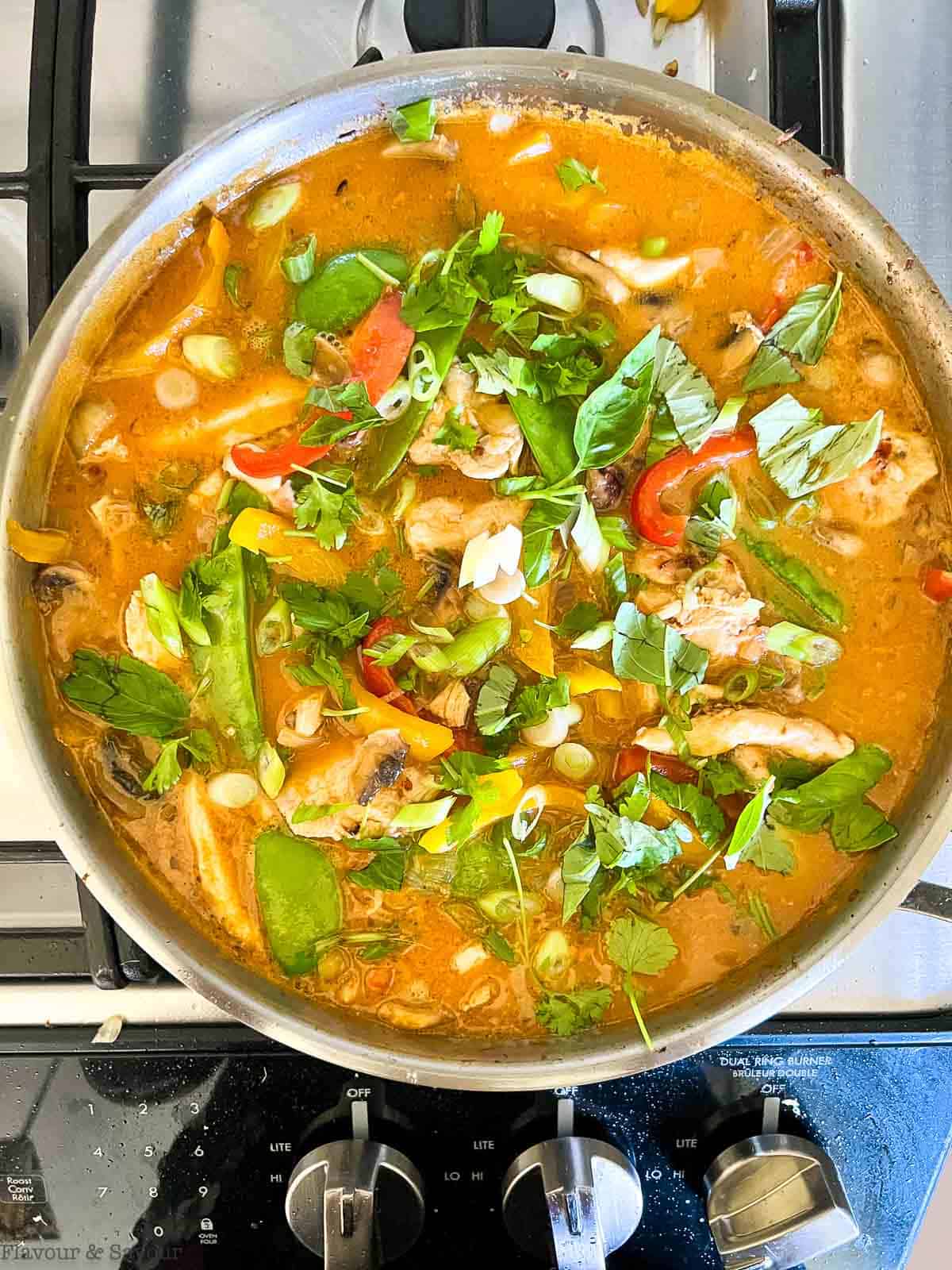 Adding vegetables into Thai red chicken curry sauce.