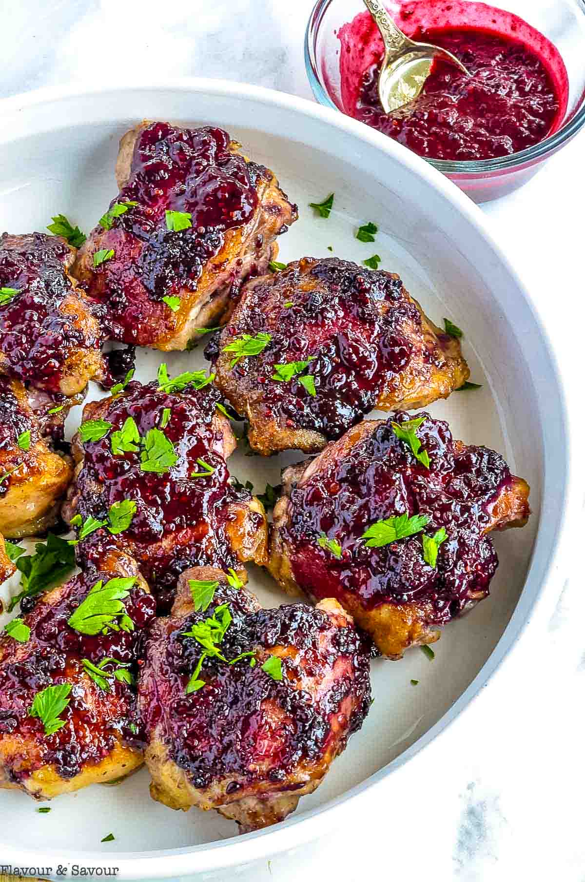 A serving dish with blackberry glazed chicken thighs and a small bowl of blackberry glaze.
