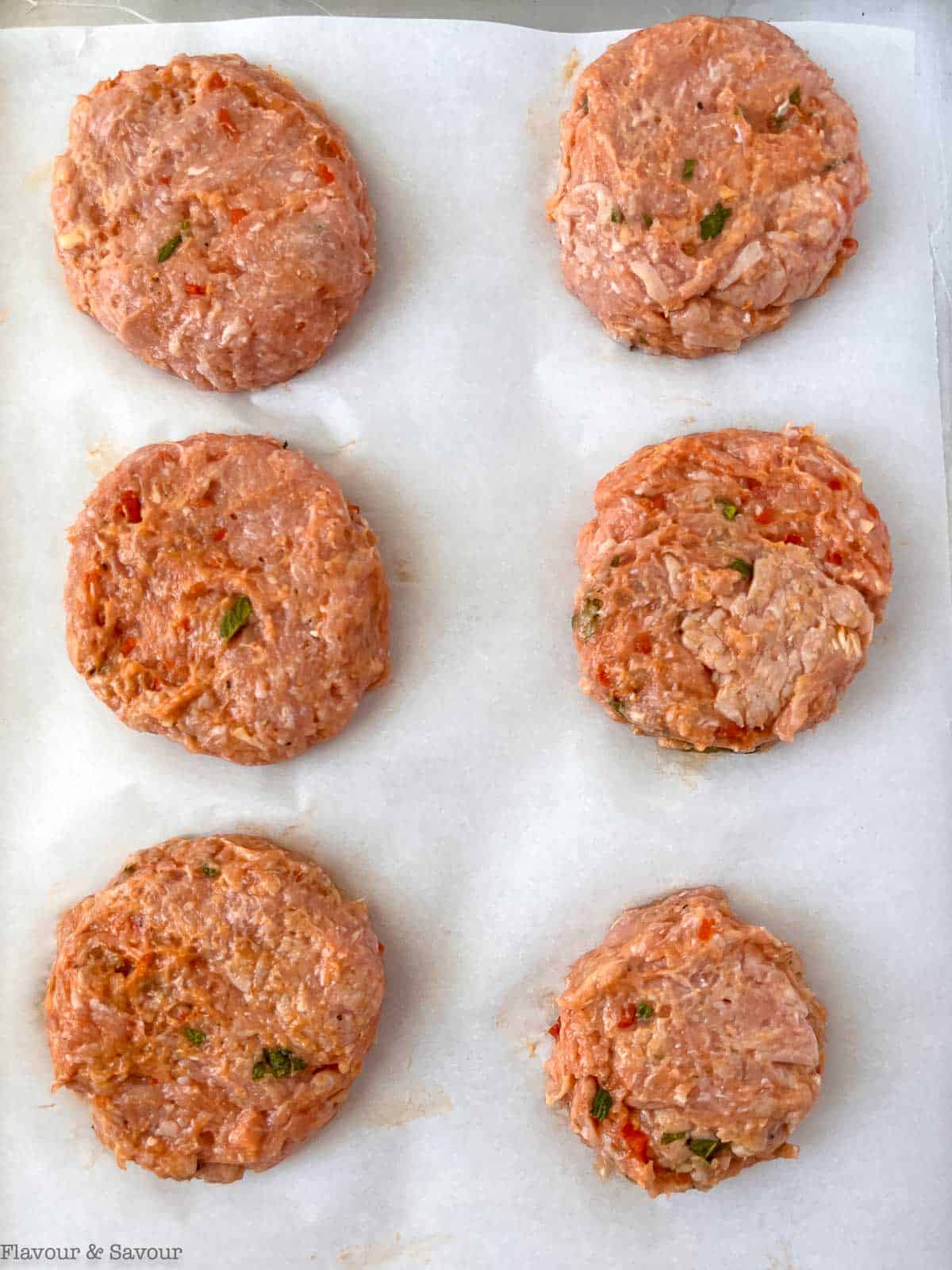 Raw chicken burgers on a sheet pan ready to freeze.