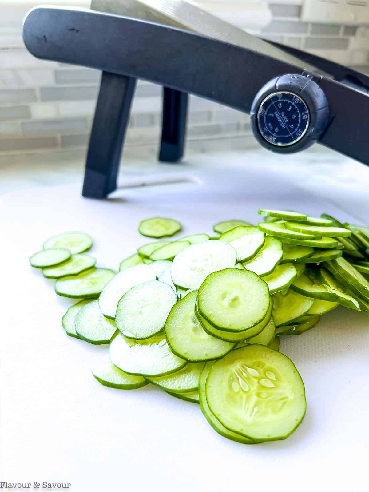 Sliced cucumbers beside a mandoline.