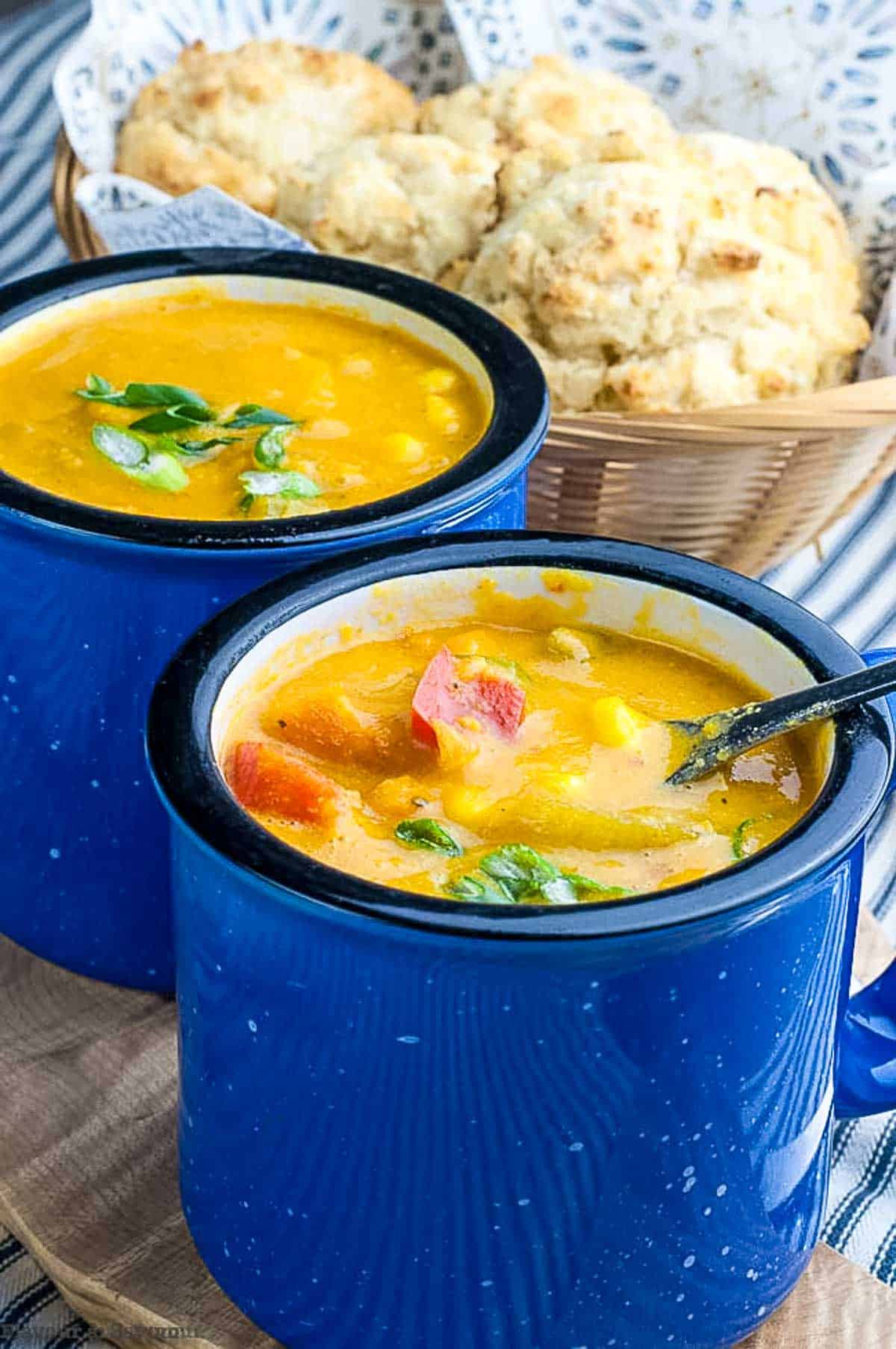 Two blue soup mugs with sweet potato corn chowder and gluten-free baking powder biscuits in the background.