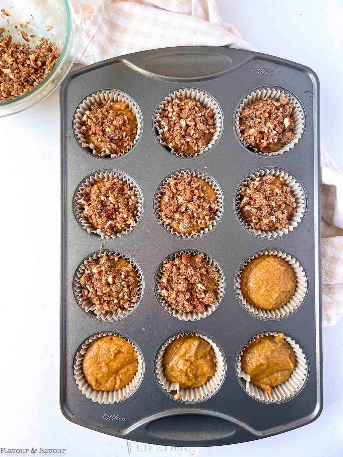 Adding streusel topping to pumpkin muffin batter in muffin tin.