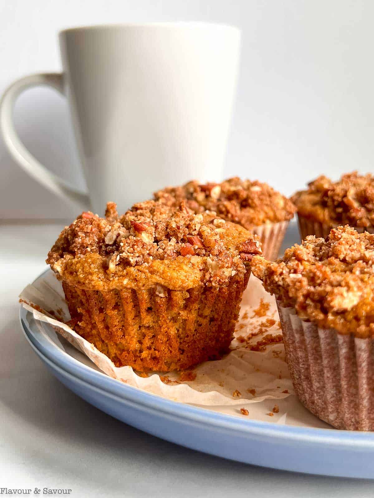 Pumpkin muffins with streusel topping on a plate with a cup of coffee.