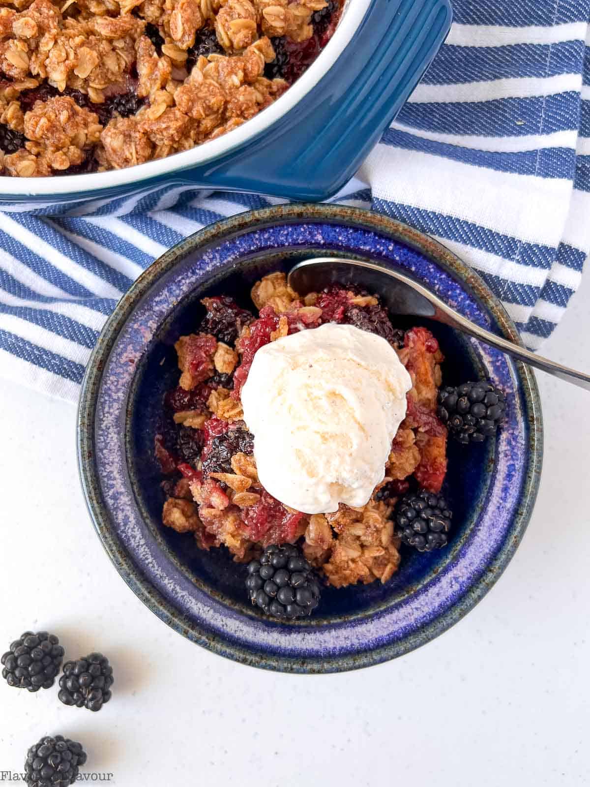 A blue pottery bowl with apple blackberry crumble and ice cream.