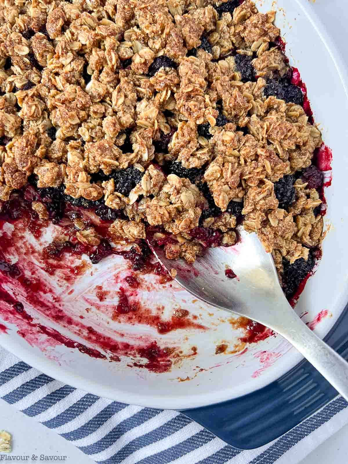 Apple Blackberry Crisp in an oval baking dish with a spoon.