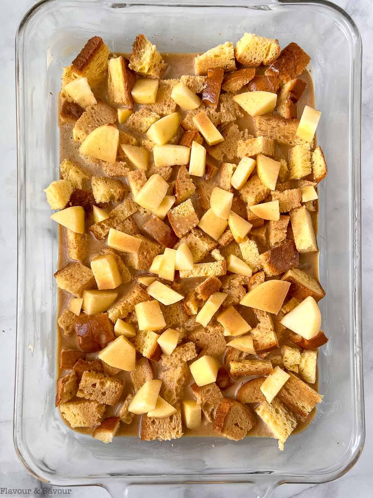 Bread, apples and custard filling layered in a casserole dish for Apple Cinnamon French Toast.