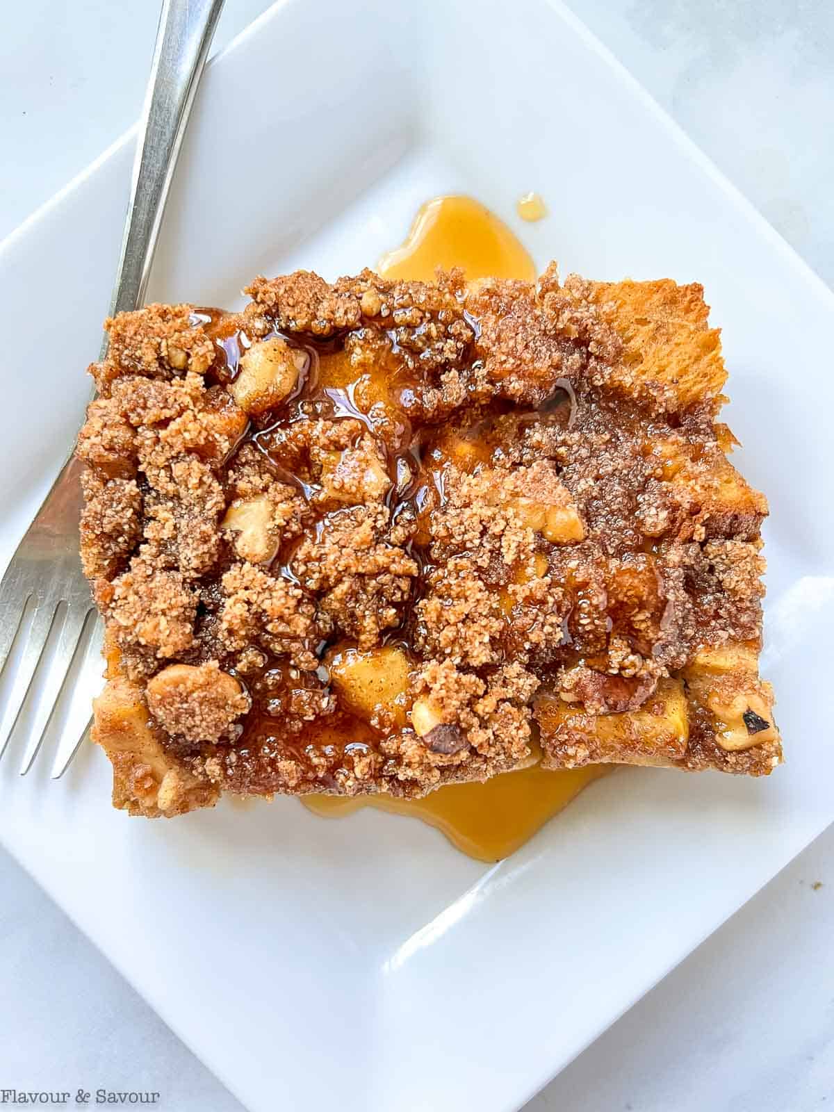 Overhead view of a square of baked French toast on a white plate with maple syrup.