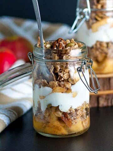 A jar of apple crumble breakfast parfait with a spoon.