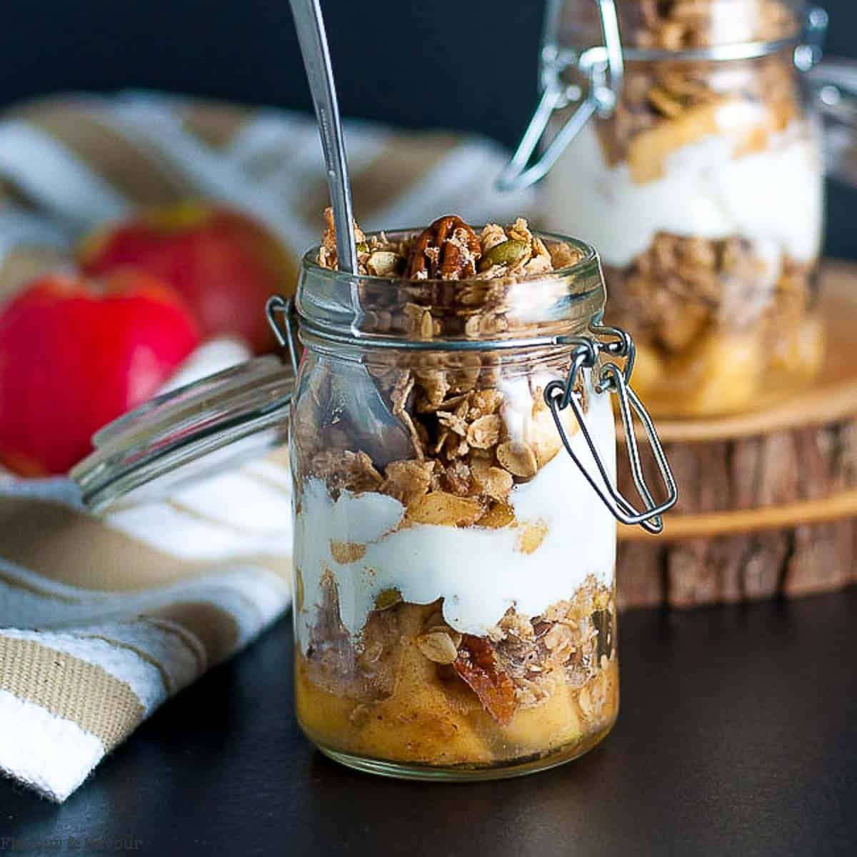 Close up view of a jar with apple crumble breakfast parfait, with layers of caramelized apples, granola and yogurt.