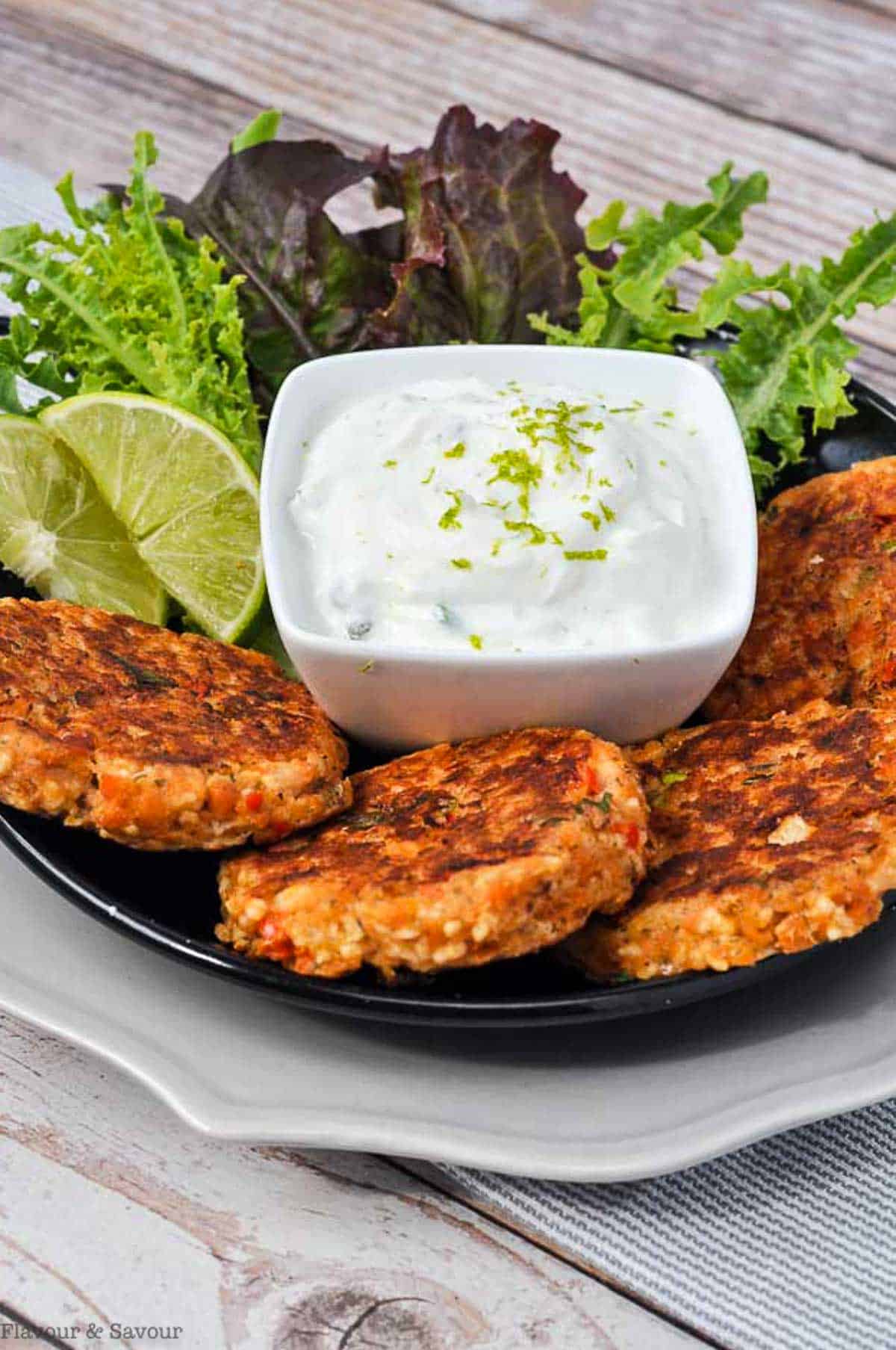 Baked Salmon Patties on a plate with Lime Dip and fresh greens.