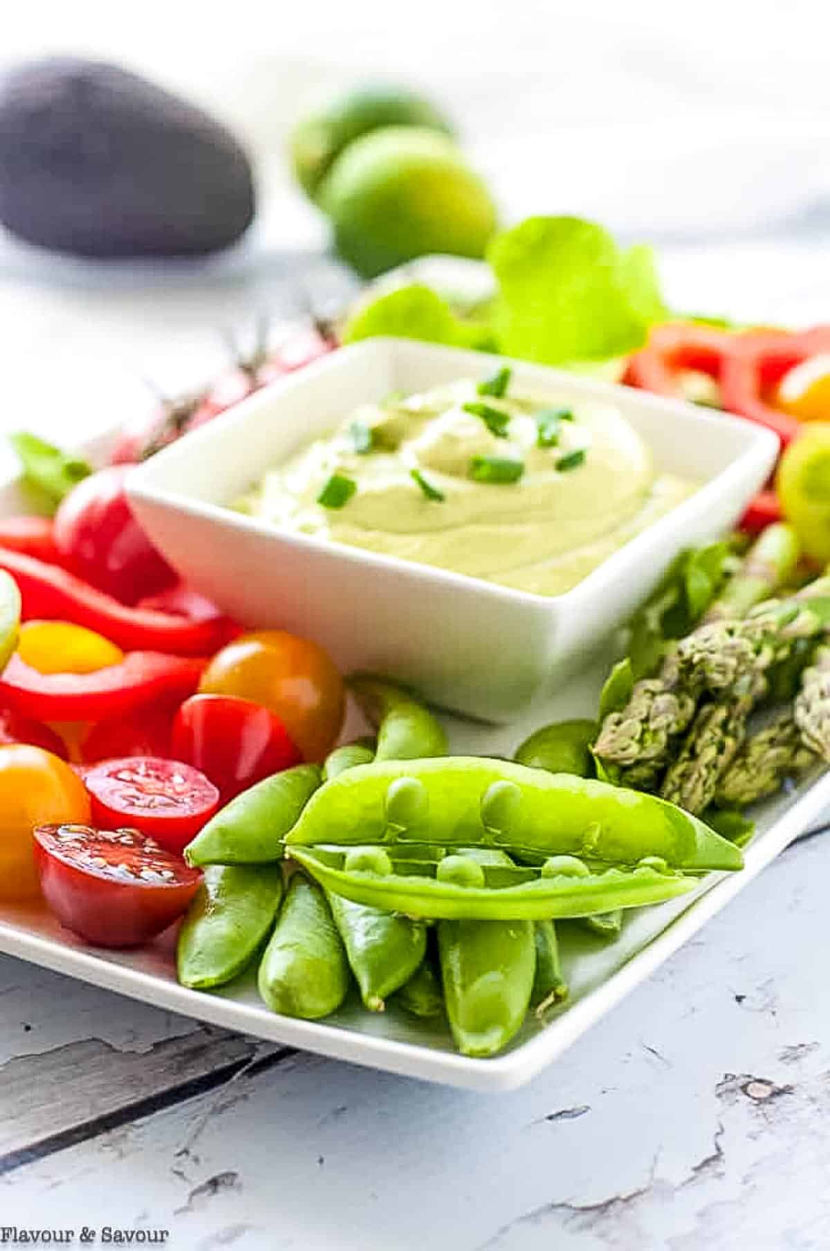 Fresh pea pods, tomatoes, asparagus and other vegetables around a dish of green goddess dip.