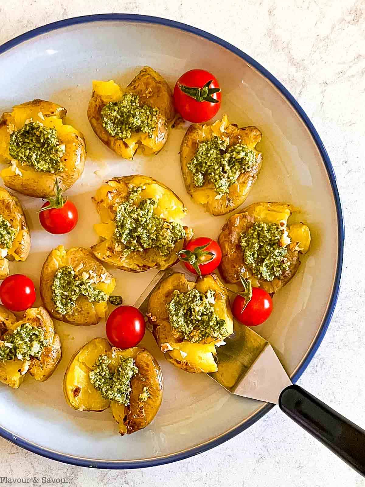 Pesto smashed potatoes on a round plate with a mini serving flipper.