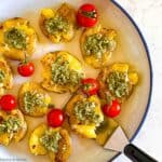 Overhead view of smashed potatoes topped with pesto sauce and served with cherry tomatoes.