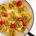 Overhead view of smashed potatoes topped with pesto sauce and served with cherry tomatoes.