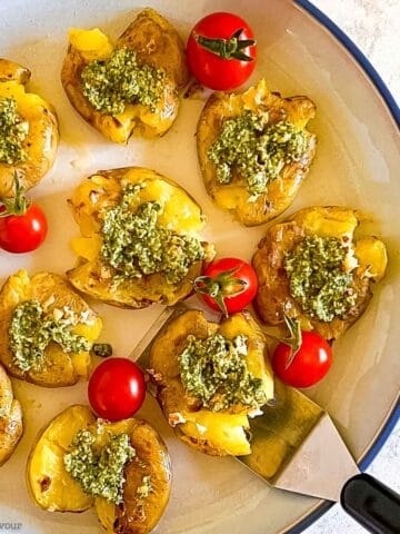 Overhead view of smashed potatoes topped with pesto sauce and served with cherry tomatoes.